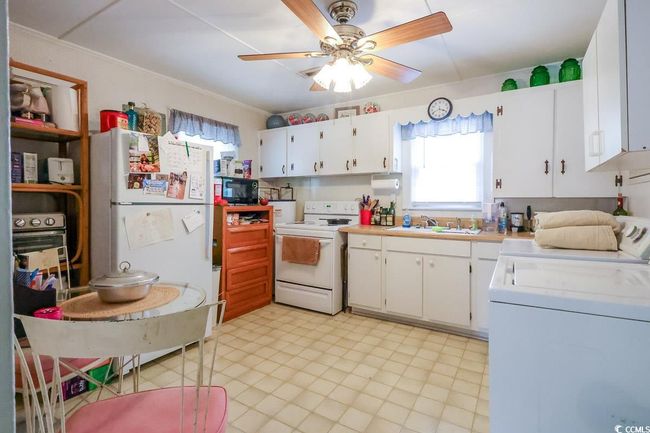 Kitchen featuring white appliances, washer / dryer, a sink, a ceiling fan, and light countertops | Image 31