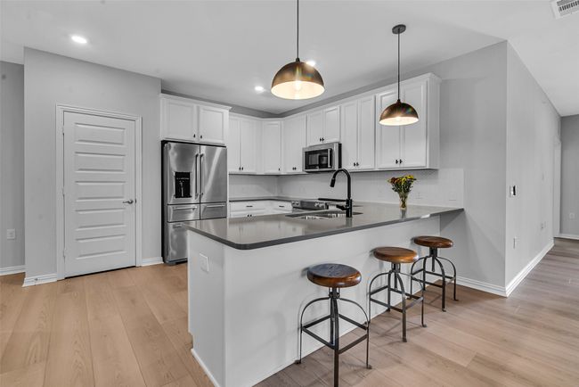 Kitchen featuring a sink, stainless steel appliances, a peninsula, and white cabinetry | Image 5