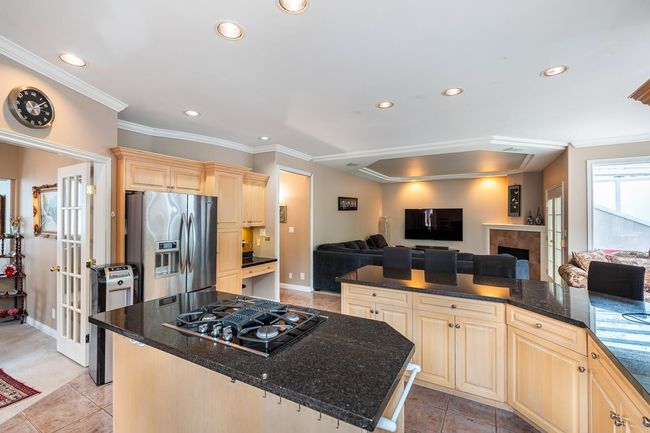 Kitchen featuring crown molding, black gas stovetop, open floor plan, light brown cabinets, and stainless steel refrigerator with ice dispenser | Image 16