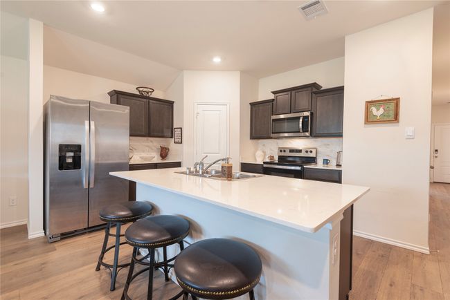 Kitchen with appliances with stainless steel finishes, decorative backsplash, light wood-style flooring, a breakfast bar area, and recessed lighting | Image 23