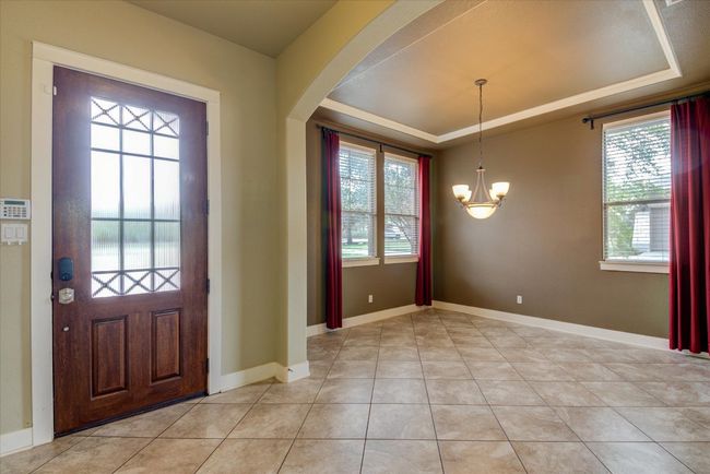 Entryway with light tile patterned floors, a notable chandelier, a tray ceiling, and a wealth of natural light | Image 6