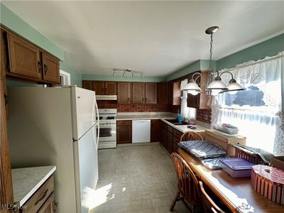 Kitchen featuring an inviting chandelier, white appliances, pendant lighting, backsplash, and sink | Image 3