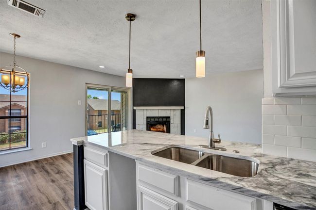 Kitchen with white cabinetry, sink, hanging light fixtures, light stone counters, and a tiled fireplace | Image 8