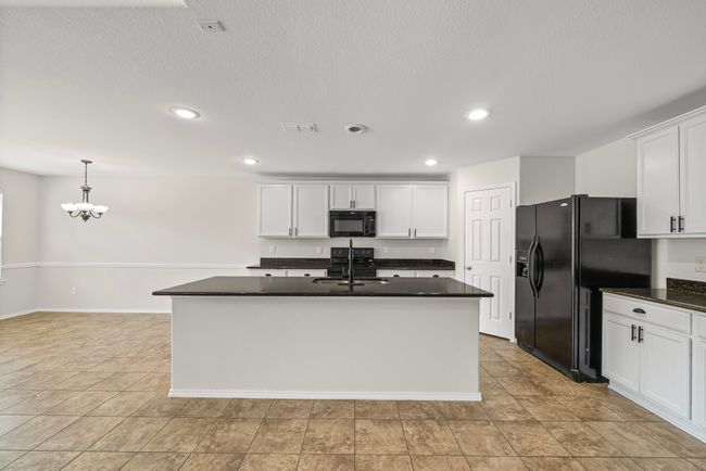 Kitchen featuring black appliances, dark countertops, white cabinetry, a chandelier, and a kitchen island with sink | Image 13