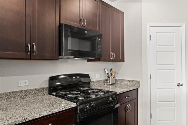 Kitchen with black appliances, dark brown cabinets, and light stone counters | Image 12