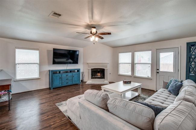 Living area featuring ceiling fan, a fireplace with raised hearth, dark wood-style floors, and baseboards | Image 4