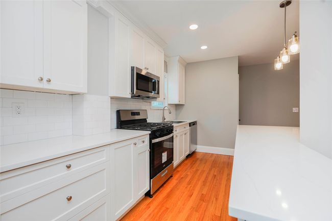 Kitchen featuring tasteful backsplash, a sink, light wood-type flooring, white cabinetry, and stainless steel appliances | Image 15