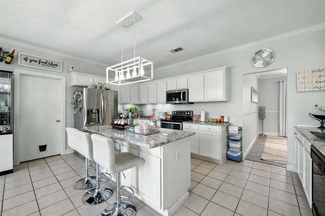 Kitchen featuring appliances with stainless steel finishes, light tile patterned floors, crown molding, a kitchen island, and white cabinets | Image 15
