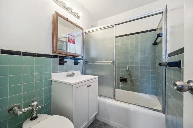 Bathroom featuring toilet, combined bath / shower with glass door, tile walls, and vanity | Image 11