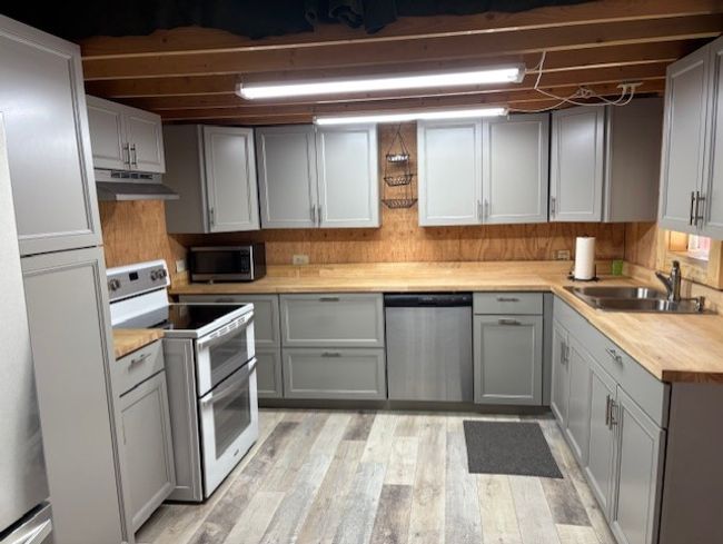 Kitchen with stainless steel appliances, under cabinet range hood, a sink, light laminate-style floors, and gray cabinetry | Image 13