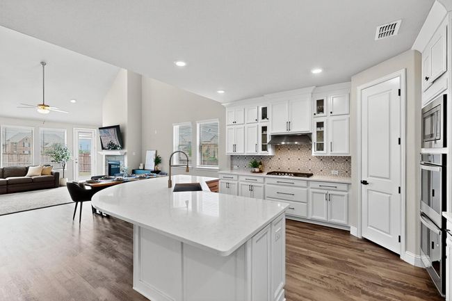 Kitchen featuring glass insert cabinets, decorative backsplash, open floor plan, white cabinets, and light stone countertops | Image 7