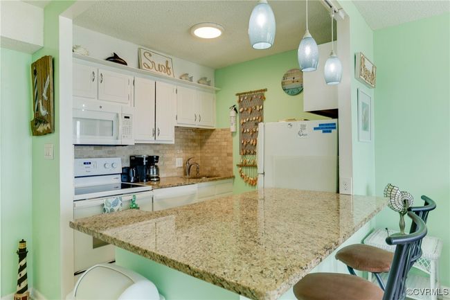 Kitchen with white appliances, a breakfast bar, a sink, white cabinets, and tasteful backsplash | Image 5