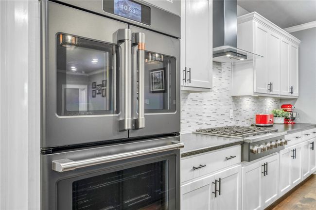 Kitchen featuring white cabinetry, backsplash, ornamental molding, stainless steel appliances, and wall chimney range hood | Image 18