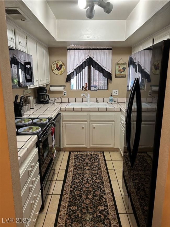 Kitchen with tile countertops, a tray ceiling, refrigerator, and stove | Image 12
