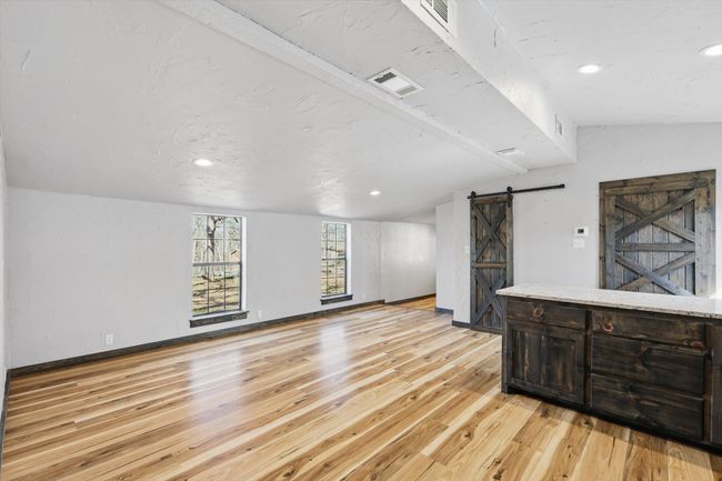 Living area featuring visible vents, light wood-style flooring, lofted ceiling with beams, a barn door, and baseboards | Image 18