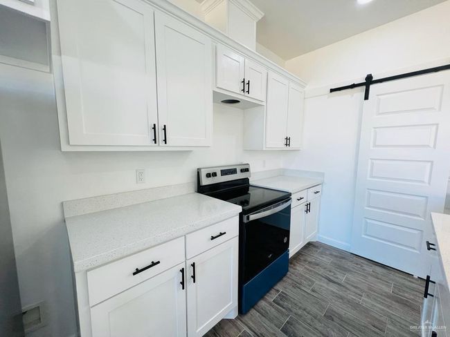 Kitchen with a barn door, white cabinets, and stainless steel range with electric stovetop | Image 6