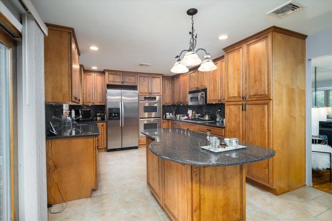 Kitchen with appliances with stainless steel finishes, brown cabinets, light tile patterned flooring, a center island, and recessed lighting | Image 6