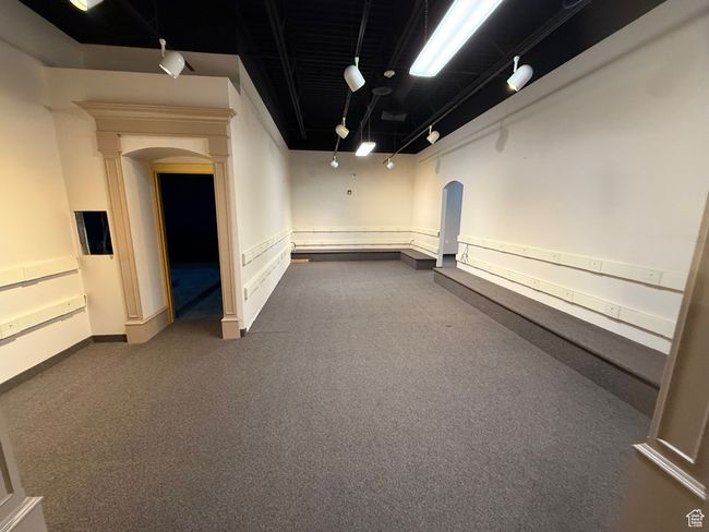 Finished below grade area featuring arched walkways, baseboards, dark colored carpet, and track lighting | Image 14