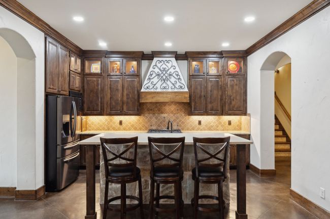 Bar with arched walkways, baseboards, black stainless steel fridge, andtravertinel backsplash | Image 7