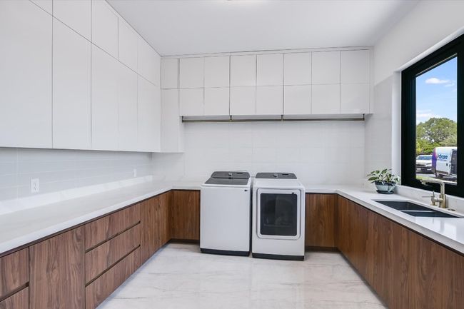 Incredible Laundry room featuring washer and clothes dryer, light marble look tile floors, and loads of cabinet as well as a sink and window | Image 21