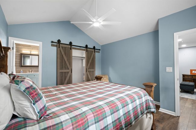 Bedroom featuring a barn door, wood finished floors, vaulted ceiling, baseboards, and ceiling fan | Image 17