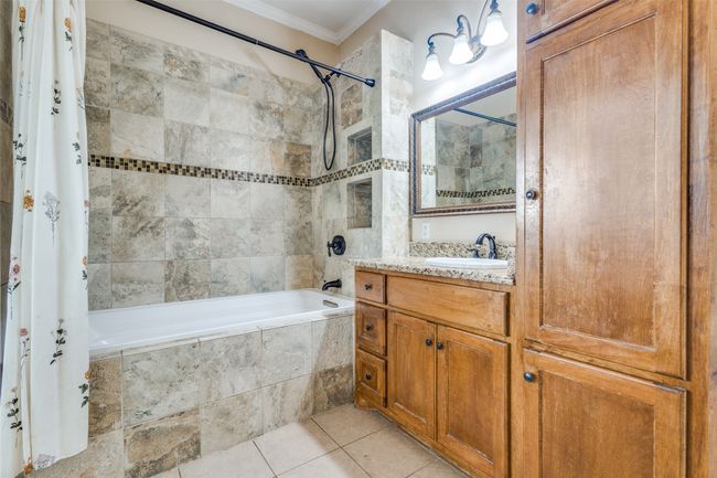 The primary bathroom ensuite features ornamental molding, deep soaking bath/shower combo, with added granite counter-top vanity storage, and tile patterned floors | Image 14