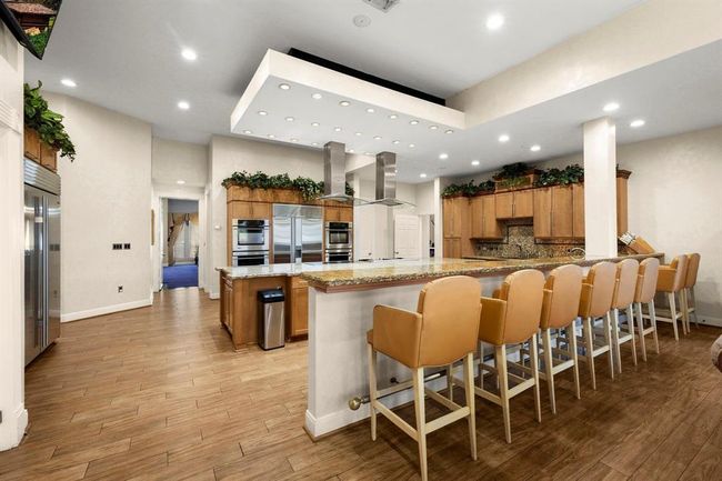 This photo features a spacious modern kitchen with stainless steel appliances, ample cabinetry, a large island with seating, and sleek recessed lighting, perfect for entertaining and cooking. | Image 9