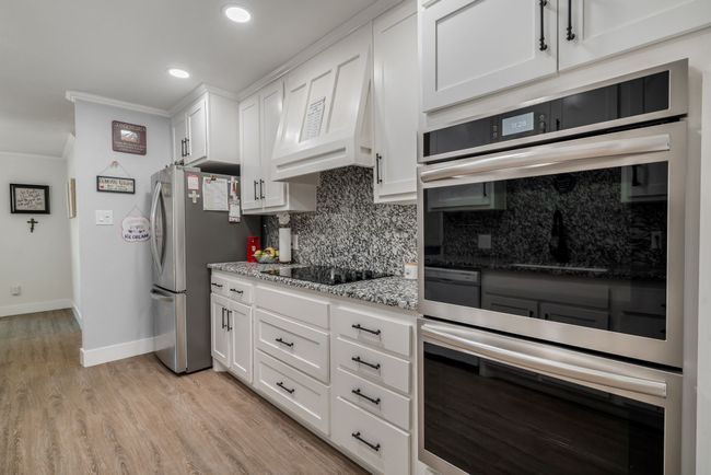 Kitchen with crown molding, stainless steel appliances, decorative backsplash, white cabinetry, and light stone countertops | Image 8