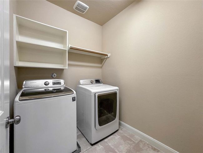 This photo shows a compact laundry room with a washer and dryer, a shelf for storage, and neutral-colored walls and flooring. | Image 30