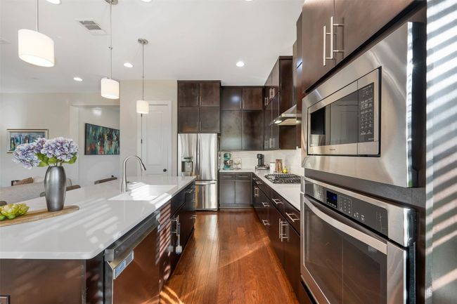 Kitchen with appliances with stainless steel finishes, dark brown cabinets, dark wood finished floors, light countertops, and decorative light fixtures | Image 28