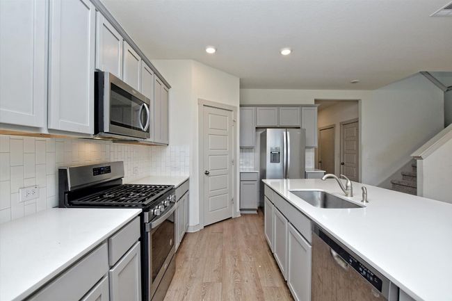 Kitchen with appliances with stainless steel finishes, a sink, light wood-type flooring, gray cabinets, and light countertops | Image 12