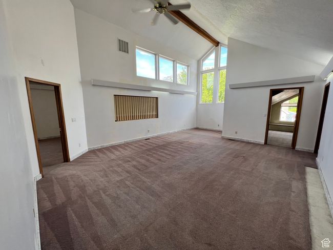 Unfurnished living room featuring carpet flooring, high vaulted ceiling, beamed ceiling, a ceiling fan, and baseboards | Image 7