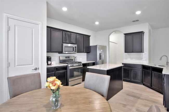 Kitchen with appliances with stainless steel finishes, a sink, light wood-type flooring, light stone countertops, and arched walkways | Image 7