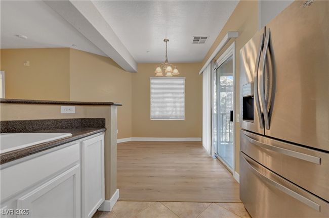 Kitchen featuring an inviting chandelier, light tile patterned floors, stainless steel fridge with ice dispenser, pendant lighting, and visible vents | Image 12