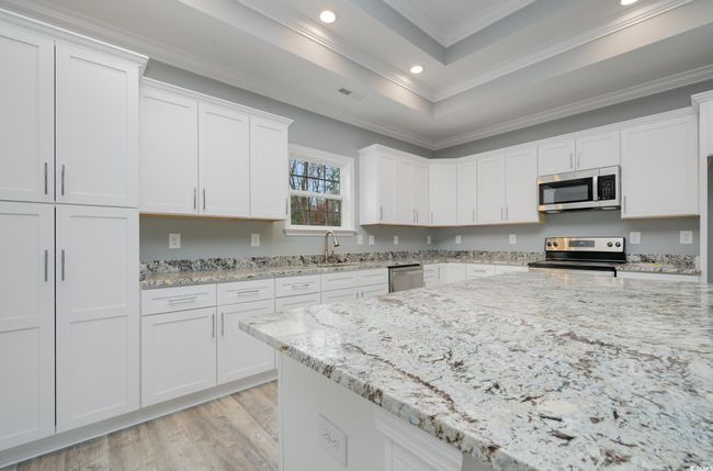 Kitchen with white cabinets, stainless steel appliances, light stone countertops, and crown molding | Image 7