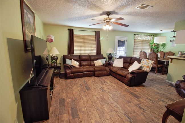 Living room featuring a ceiling fan, wood finished floors, a textured ceiling, and visible vents | Image 5
