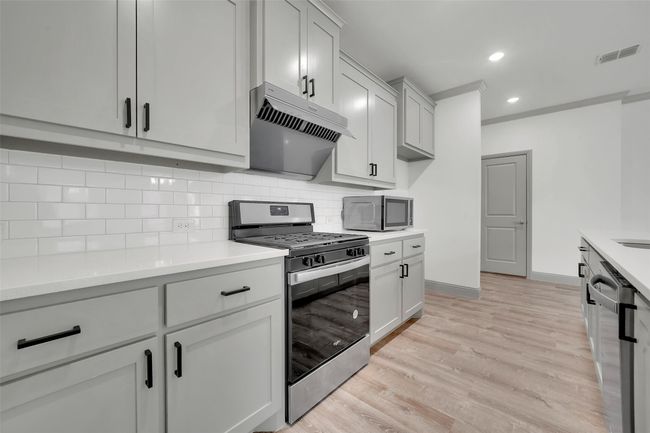 Kitchen with tasteful backsplash, visible vents, appliances with stainless steel finishes, under cabinet range hood, and light wood-style flooring | Image 11