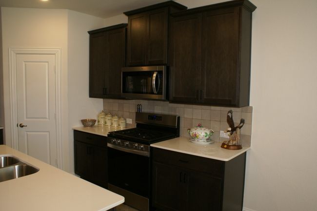 Kitchen featuring decorative backsplash, light countertops, dark brown cabinets, and stainless steel appliances | Image 14