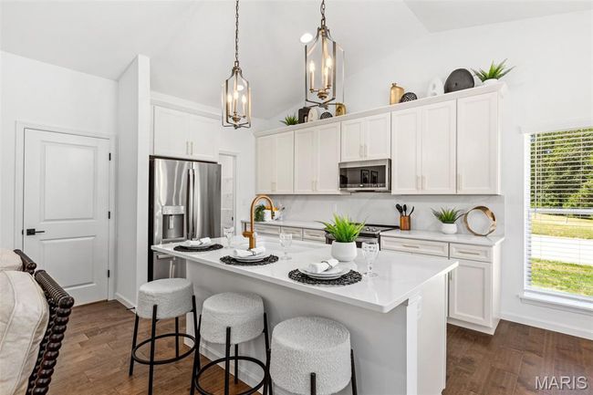Kitchen featuring stainless steel appliances, lofted ceiling, a kitchen bar, light countertops, and white cabinetry | Image 12