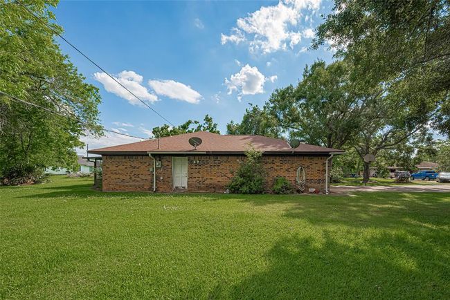 This is a one-story brick home with a spacious lawn and mature trees, offering peaceful and private setting. The roof is sloped, and there's a driveway with ample parking space. Ideal for those seeking a serene residential area. | Image 36