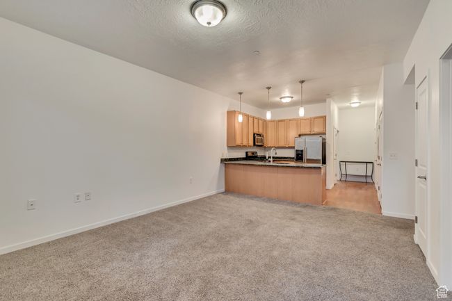 Kitchen with open floor plan, stainless steel appliances, dark countertops, a peninsula, and light carpet | Image 8
