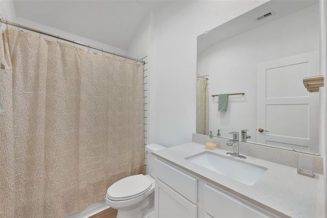 This bathroom features a clean, modern design with a white vanity, quartz countertop, and a large mirror. It includes a shower with a beige curtain, neutral walls, and contemporary fixtures, creating a bright and inviting space. | Image 20