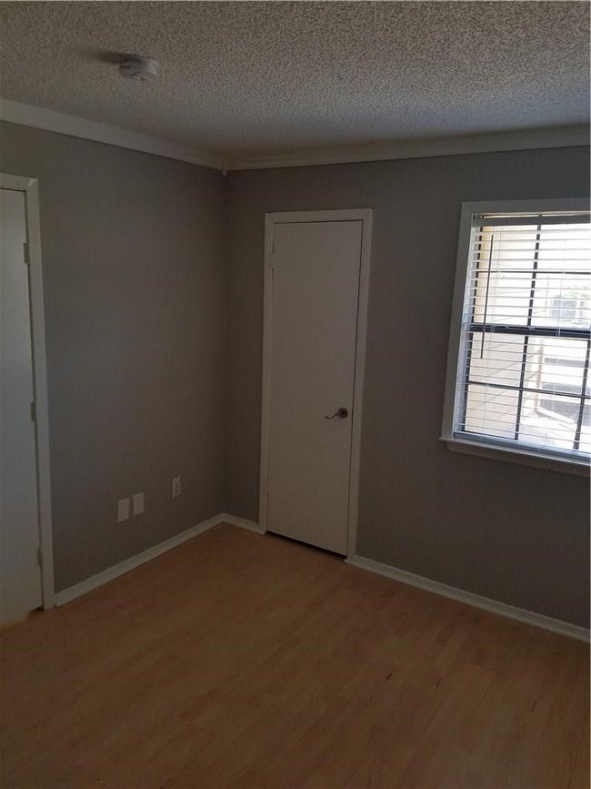 Unfurnished room featuring light wood finished floors, a textured ceiling, ornamental molding, baseboards, and a smoke detector | Image 10