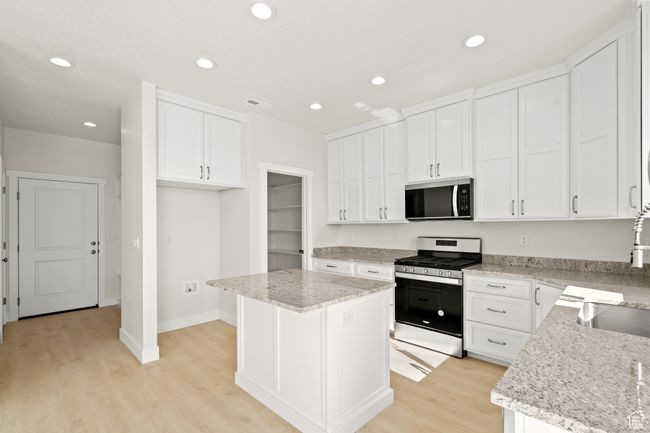 Kitchen with stainless steel appliances, white cabinets, recessed lighting, a center island, and light wood-style floors | Image 9