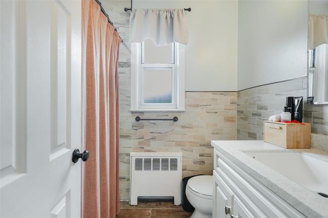 Bathroom with radiator, toilet, vanity, tile walls, and a shower with curtain | Image 10