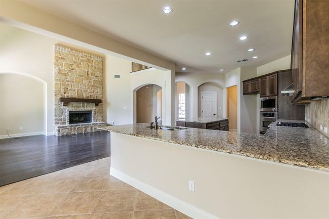 Kitchen with recessed lighting, light stone counters, stainless steel appliances, a sink, and dark brown cabinetry | Image 14