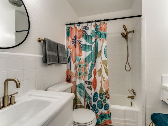 Bathroom with tile walls, vanity, toilet, and shower / bath combo with shower curtain | Image 8