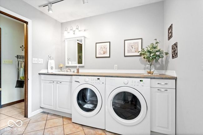 laundry room featuring washing machine and clothes dryer, rail lighting, cabinet space, and light tile patterned floors | Image 20