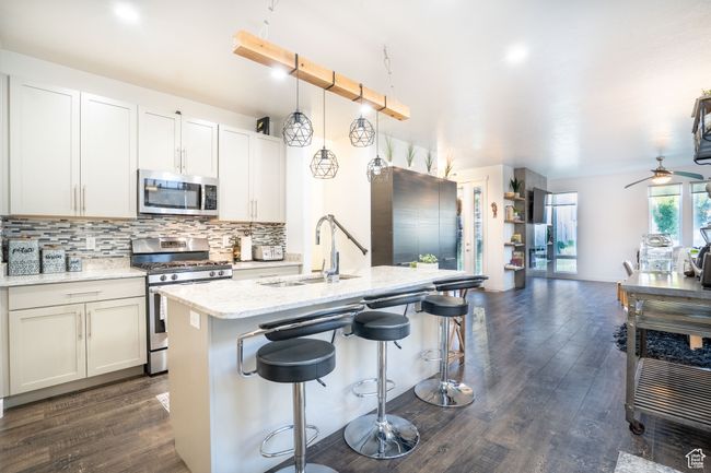Kitchen featuring appliances with stainless steel finishes, open floor plan, decorative backsplash, dark wood-type flooring, and a breakfast bar area | Image 5
