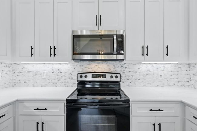Kitchen with stainless steel microwave, black / electric stove, light countertops, and white cabinets | Image 12
